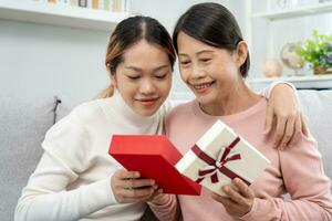 madre giorno, carino asiatico adolescente ragazza dare regalo scatola per maturo mezzo età mamma. amore, bacio, cura, contento Sorridi godere famiglia volta. festeggiare speciale occasione, contento compleanno, contento nuovo anni, allegro Natale foto