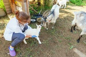 giovane veterinario donna con stetoscopio Tenere e l'esame capra ragazzo su ranch sfondo. giovane goatling nel veterinario mani per dai un'occhiata su nel naturale eco azienda agricola. moderno animale bestiame, ecologico agricoltura. foto