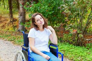 giovane contento handicap donna nel sedia a rotelle su strada nel ospedale parco in attesa per paziente Servizi. paralizzato ragazza nel non valido sedia per Disabilitato persone all'aperto nel natura. reinserimento concetto. foto