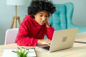 africano americano ragazza utilizzando il computer portatile a casa ufficio guardare a schermo digitando chat lettura scrittura e-mail. giovane donna avendo virtuale incontro in linea Chiacchierare video chiamata conferenza opera apprendimento a partire dal casa foto