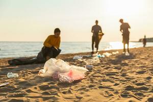 terra giorno. volontari attivisti raccoglie spazzatura pulizia di spiaggia costiero zona. donna e mans mette plastica spazzatura nel spazzatura Borsa su oceano costa. ambientale conservazione costiero zona pulizia. foto