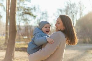 contento famiglia all'aperto. madre Abbracciare una persona sua bambino all'aperto. mamma sollevamento nel aria poco bambino piccolo bambino figlio. donna e poco bambino ragazzo riposo a piedi nel parco. madre abbracci bambino con amore cura. foto