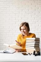 giovane donna sorridente in maglione giallo che legge un libro e ride foto