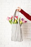 mano di donna che tiene borsa in tessuto a pois grigi con tulipani colorati foto