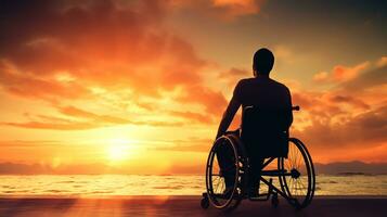 silhouette di Disabilitato uomo su sedia a rotelle a il spiaggia durante tramonto, disattivare giorno foto