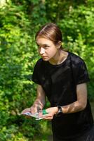 giovane ragazza nel foresta lettura carta geografica e ricerca per un' controllo punto. gli sport orientamento concorrenza. foto