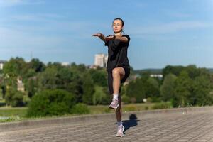 giovane, in forma e sportivo ragazza nel nero Abiti allungamento dopo il allenarsi nel il urbano città parco. foto