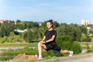 giovane, in forma e sportivo ragazza nel nero Abiti allungamento dopo il allenarsi nel il urbano città parco. foto