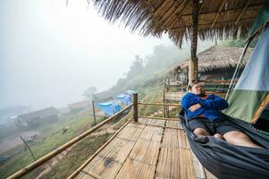 asiatico Grasso viaggiatore addormentato su amaca su il di legno balcone con bellissimo paesaggio e nebbia nel il mattina di sapan villaggio nan thailand.sapan è piccolo e tranquillo villaggio nel il montagna. foto