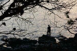 uomo retroilluminato con un' pesca asta nel il mare foto