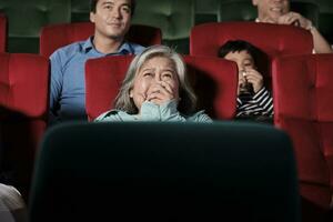 vario persone nel Teatro. anziano asiatico donna e multirazziale pubblico siamo impaurito di Guardando thriller e orrore cinema, spaventato insieme di film, e divertimento stile di vita con film arte mostrare. foto