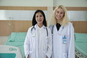 professionale medico personale partner, Due bianca in uniforme femmina medici Guarda a telecamera, allegro e sorridente, contento fisico opera occupazione nel ospedale clinica. foto