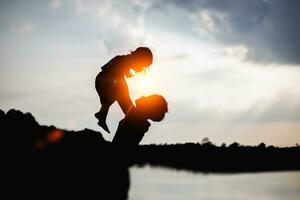 un' silhouette di un' contento giovane madre armonioso famiglia all'aperto. ridendo e giocando nel il estate su il tramonto background.sstkhome foto