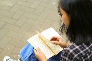 contento e succes femmina asiatico Università alunno godendo leggere un' libro nel il parco foto