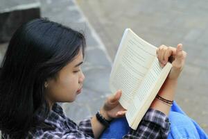 contento e succes femmina asiatico Università alunno godendo leggere un' libro nel il parco foto