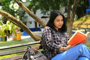 contento e succes femmina asiatico Università alunno godendo leggere un' libro nel il parco foto