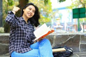 contento allegro asiatico femmina alunno lettura un' libro e ridendo godendo vacanza foto