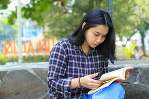 grave asiatico donna alunno leggere un' libro pensare e fare ricerca per sua compiti a casa foto