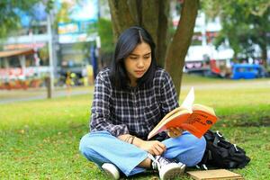 grave asiatico donna alunno leggere un' libro pensare e fare ricerca per sua compiti a casa foto