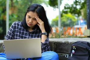 esausto e stressato asiatico donna alunno Lavorando utilizzando il computer portatile e studia con testo libri nel all'aperto foto