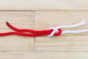 nodo piegato in lamiera realizzato con corda rossa su fondo in legno. foto