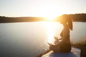 la giovane donna in buona salute sta praticando lo yoga al lago di montagna durante il tramonto. foto