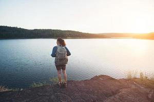 giovane donna escursionista in piedi sulla roccia e godersi il tramonto sul lago.