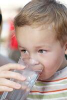 poco ragazzo bere un' bicchiere di fresco acqua foto