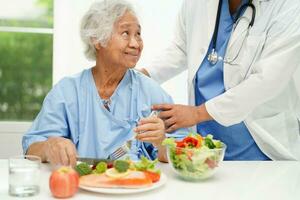 asiatico anziano donna paziente mangiare salmone palo e verdura insalata per salutare cibo nel Ospedale. foto