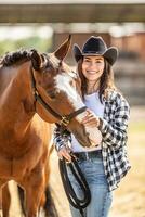 bella vista giovane donna nel cowboy cappello colpi un' cavallo su braciole mentre sorridente a il telecamera foto