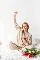 donna seduta sul letto in pigiama con in mano un bicchiere di vino foto