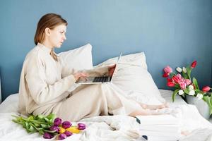 donna seduta sul letto che indossa il bouquet del pigiama che chiacchiera sul laptop foto