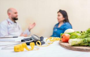 dietologo uomo con donna paziente nel ufficio. dietologo parlando per femmina paziente con messa a fuoco su il frutta nel il primo piano. concetto di dietologo consulenza femmina cliente foto