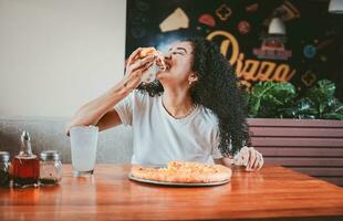 stile di vita di dai capelli afro donna godendo un' Pizza nel un' ristorante. contento afro capelli donna mangiare Pizza nel un' ristorante foto