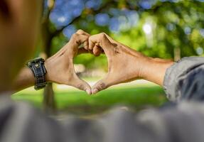 vicino su di Due mani insieme nel un' cuore forma, mani insieme nel un' cuore forma, giovane uomo mettendo dita insieme nel un' cuore forma foto