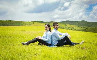 coppia nel amore nel il campo seduta indietro per indietro guardare a il il telecamera, giovane rilassato coppia seduta nel il campo con loro schiene per ogni altro lon il campo foto