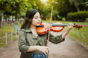 donna giocando il violino nel il strada. vicino su di violinista ragazza giocando nel un' parco. artista donna giocando il violino all'aperto, donna giocando il violino nel un' simpatico parco. violinista donna concetto foto