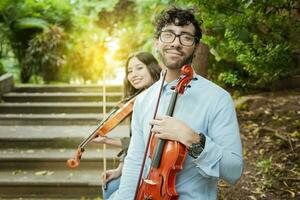 ritratto di Due giovane violisti seduta fuori. uomo e donna violinista seduta su il scale. concetto di Due giovane violinisti, Due giovane violinisti seduta all'aperto guardare a il telecamera foto