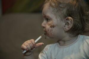 bambino ragazza mangiare sua cioccolato deserto con un' cucchiaio e fabbricazione un' pasticcio foto