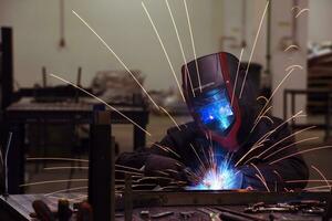 saldatore professionista dell'industria pesante che lavora all'interno della fabbrica, indossa il casco e inizia a saldare. messa a fuoco selettiva foto