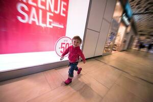 poco ragazza in esecuzione attraverso shopping centro commerciale foto