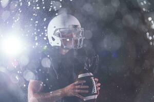 americano calcio campo solitario atleta guerriero in piedi su un' campo detiene il suo casco e pronto per giocare a. giocatore preparazione per correre, attacco e Punto touchdown. piovoso notte con drammatico nebbia, blu leggero foto