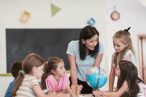 femmina insegnante con bambini nel geografia classe guardare a globo. lato Visualizza di gruppo di diverso contento scuola bambini con globo nel aula a scuola. foto
