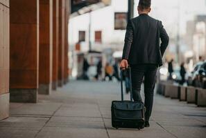 andando per aeroporto terminale. fiducioso uomo d'affari viaggiatore a piedi su città strade e traino il suo valigia potabile caffè e A proposito di su smartphone foto