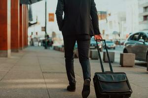 andando per aeroporto terminale. fiducioso uomo d'affari viaggiatore a piedi su città strade e traino il suo valigia potabile caffè e A proposito di su smartphone foto