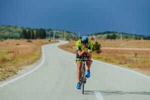 pieno lunghezza ritratto di un attivo triatleta nel abbigliamento sportivo e con un' protettivo casco equitazione un' bicicletta. selettivo messa a fuoco foto