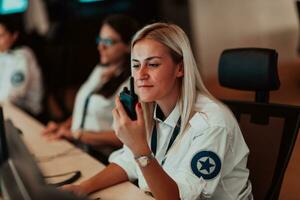 femmina sicurezza operatore Tenere portatile Radio nel mano mentre Lavorando nel un' dati sistema controllo camera uffici tecnico operatore Lavorando a stazione di lavoro con multiplo mostra, sicurezza guardia Lavorando su foto