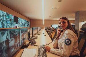 femmina sicurezza guardia operatore parlando su il Telefono mentre Lavorando a stazione di lavoro con multiplo viene visualizzato sicurezza guardie ✔ Lavorando su multiplo monitor foto