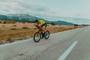 pieno lunghezza ritratto di un attivo triatleta nel abbigliamento sportivo e con un' protettivo casco equitazione un' bicicletta. selettivo messa a fuoco foto