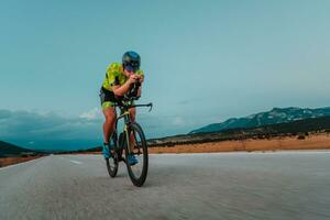 pieno lunghezza ritratto di un attivo triatleta nel abbigliamento sportivo e con un' protettivo casco equitazione un' bicicletta. selettivo messa a fuoco foto